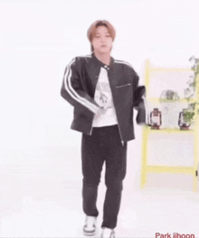 a young man wearing a black jacket and black pants is standing in front of a yellow shelf .