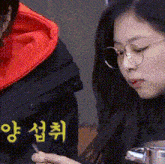 a woman wearing glasses is looking at her phone while a man wearing an orange hoodie looks on .