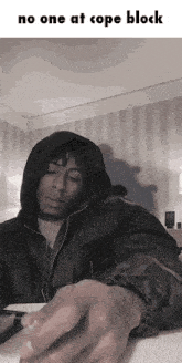 a man in a hooded jacket is sitting at a table with the words no one at cope block above him