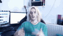 a man with long blonde hair is sitting in front of two computer monitors