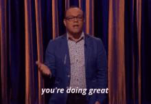 a man in a blue suit says you 're doing great in front of a curtain