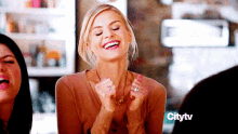 a woman is laughing with her hands in the air while sitting at a table with two other women .