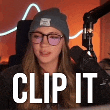 a woman wearing glasses and a beanie is standing in front of a microphone and says clip it