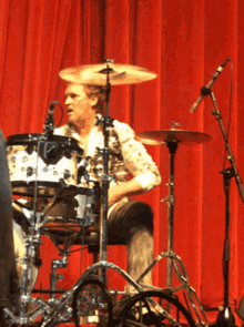 a man playing a drum set in front of a red curtain
