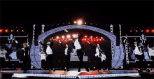 a group of men are dancing on a stage in front of a large arch