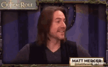 a man with long hair and a beard is smiling in front of a sign that says critical role