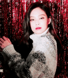 a woman wearing a sweater is standing in front of a red curtain