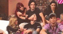 a group of people are sitting on a couch with a man covering his face with his hands .