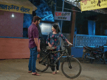 a man and a woman are standing next to a bicycle in front of a sign that says ' puja '