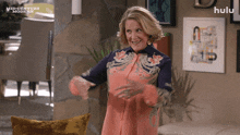 a woman is dancing in a living room with a hulu logo behind her