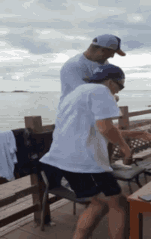 two men are standing on a deck near the ocean .