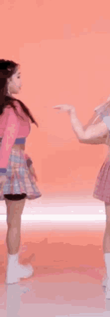 a woman in a pink sweater and plaid skirt is making a heart with her hands .