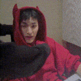 a man is wearing a red hoodie with horns on the hood .