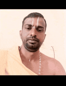 a shirtless man with a white line on his forehead looks at the camera
