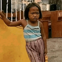 a little girl is standing in front of a yellow wall holding a toy .