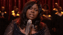 a woman singing into a silver microphone with her hand up