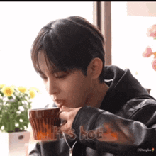 a man drinking a cup of coffee with the words " it 's hot " on the sleeve
