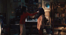 two women are fighting in a living room and one of them is wearing a pink shirt