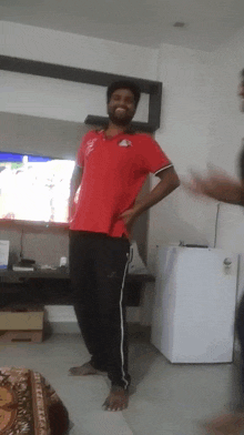 a man in a red shirt and black pants stands in front of a tv