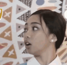 a close up of a woman 's face with her mouth open and a patterned wall in the background .