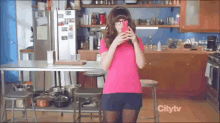 a woman in a pink shirt is standing in a kitchen with a citytv logo on the bottom