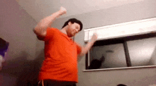 a man in an orange shirt is dancing in front of a window .