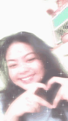 a girl is smiling and making a heart with her hands