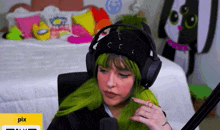 a woman with green hair is wearing headphones and a black hat .