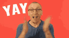 a man wearing glasses is raising his fists in the air in front of a red background with the word yay