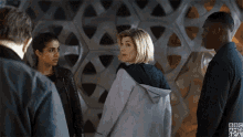 a group of people standing next to each other in front of a wall with a pattern on it .