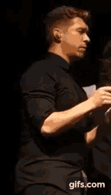 a man in a black shirt is standing in front of a sign that says ' gifs.com ' on it