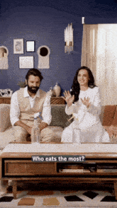 a man and a woman are sitting on a couch with a table that says who eats the most