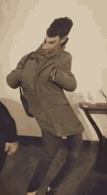 a man in a coat is dancing in a room with a table in the background .