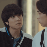 two young men are looking at each other with one wearing a necklace with the letter w on it