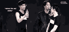 a man is holding a bottle of water and talking into a microphone while another man looks on .