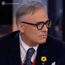 a man wearing glasses and a tie with a yellow flower pin on his jacket