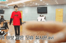 a man in a red shirt is standing in a room with korean writing on the wall