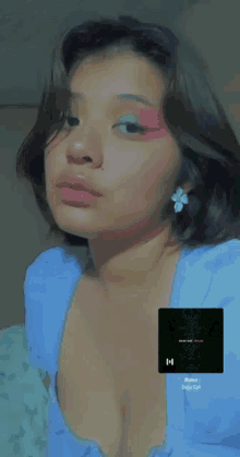a woman wearing a blue top and earrings has a picture of a song on her chest