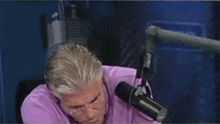 a man in a purple shirt is talking into a microphone