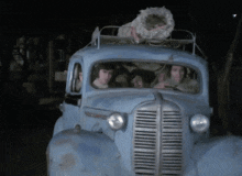 a group of people are driving a blue truck with a baby on the roof