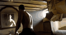 a shirtless man stands in front of a mirror looking at his reflection
