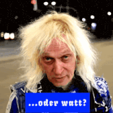 a man with blonde hair stands in front of a blue sign that says oder watt