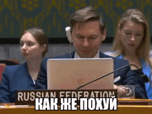 a man is sitting at a table with a laptop and a sign that says russian federation on it .