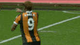 a soccer player wearing a black and orange jersey with the number 9 on the back