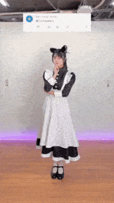 a girl in a maid costume is standing on a wooden floor with her hands on her chin .