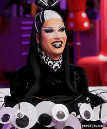 a drag queen is wearing a black and white costume with googly eyes on her arms .