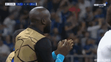a man applauds in front of a scoreboard that says int 1 0 plz