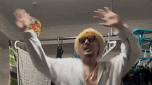 a man wearing a hat and sunglasses is standing in a laundry room with his arms outstretched .