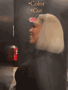 a woman with blonde hair is standing in front of a sign that says color cut and exit .