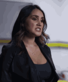 a woman wearing a black top and a black jacket has a necklace with the letter g on it